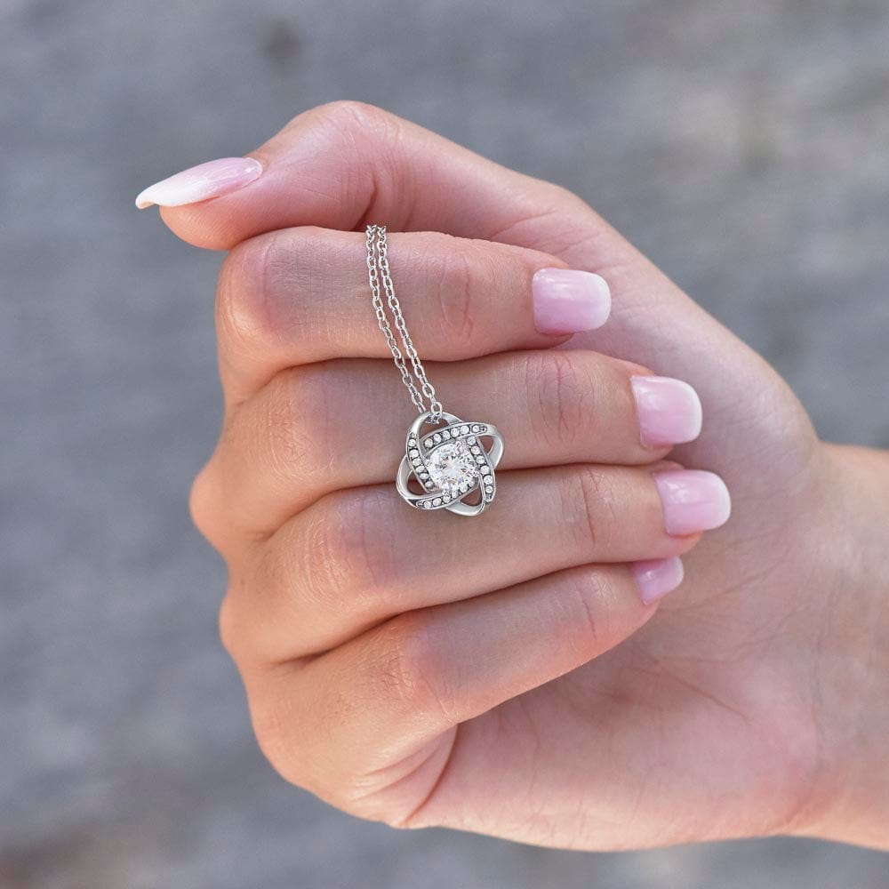 Close Up View Of Love Knot Necklace Polished Stainless Steel In Hand